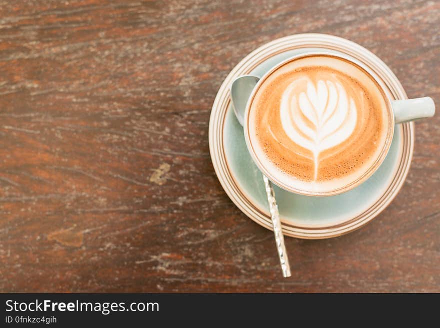 Cup and saucer with latte or cappuccino with flower design in foam on wood table. Cup and saucer with latte or cappuccino with flower design in foam on wood table.