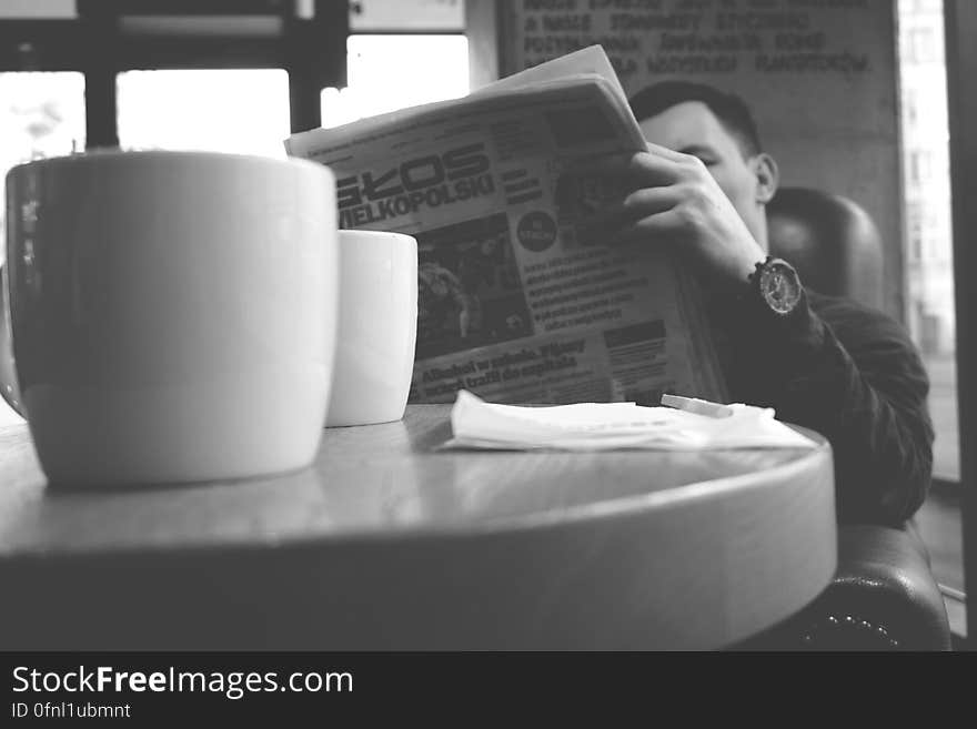 Portrait of man reading newspaper sitting at table in cafe in black and white.