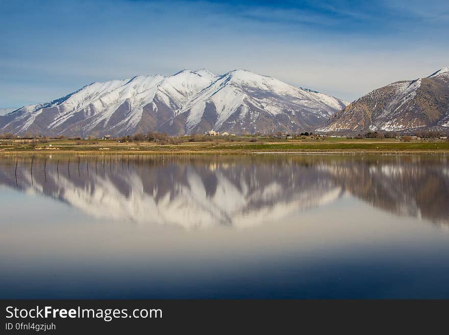 Snow capped mountain peaks reflecting in calm waters of alpine lake on sunny day. Snow capped mountain peaks reflecting in calm waters of alpine lake on sunny day.