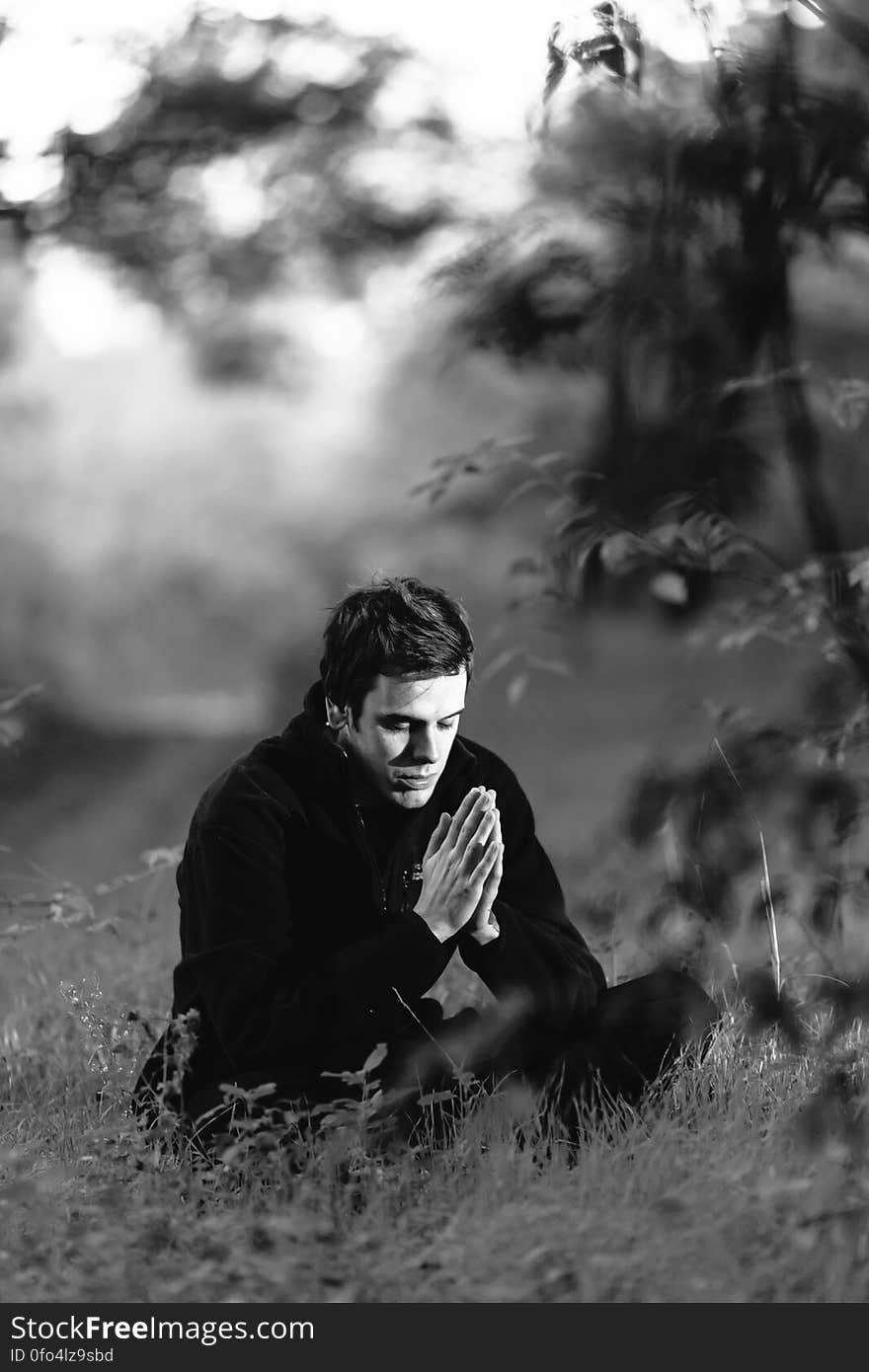 Grayscale Photography of Man Sitting on Grass Field