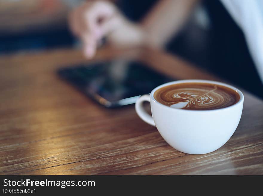 A person using a mobile phone with a cup of cappuccino on the table. A person using a mobile phone with a cup of cappuccino on the table.