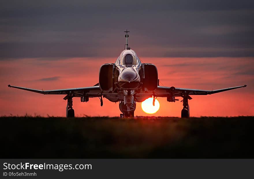 Front view of military jet aircraft on runway with orange sunset background. Front view of military jet aircraft on runway with orange sunset background.