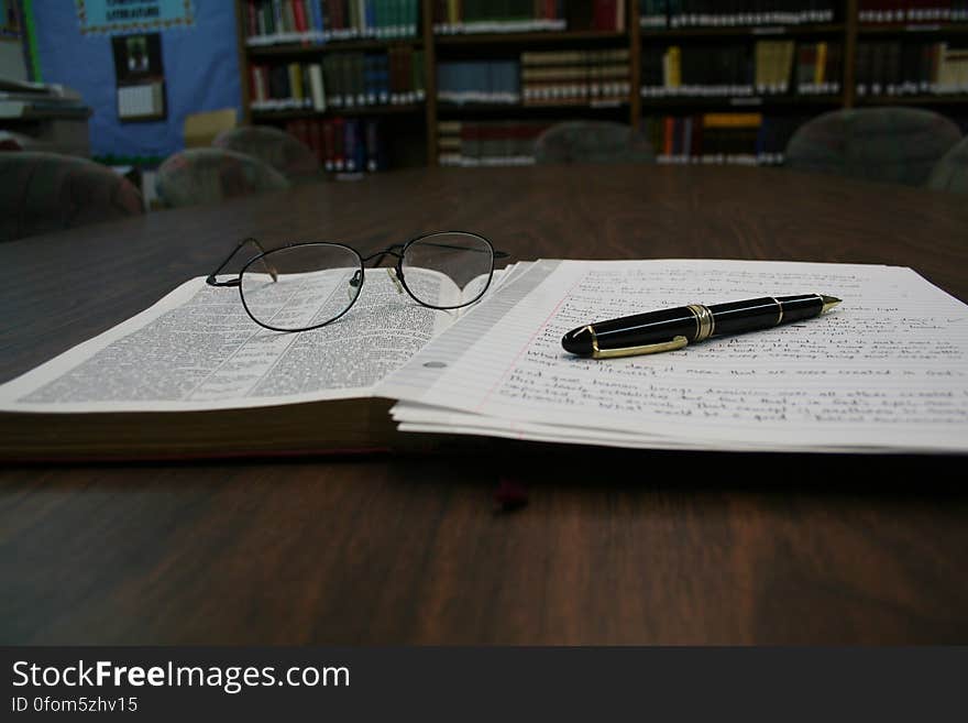 An open book with notes and eyeglasses on a library table. An open book with notes and eyeglasses on a library table.