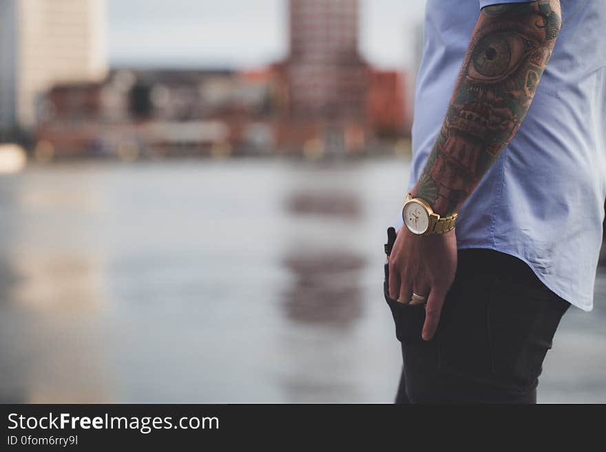 A man with tattoos standing next to water.