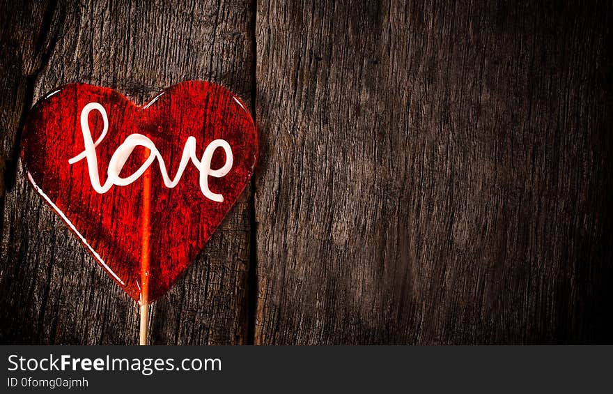 Red lollipop with word love on textured wooden background with copy space.