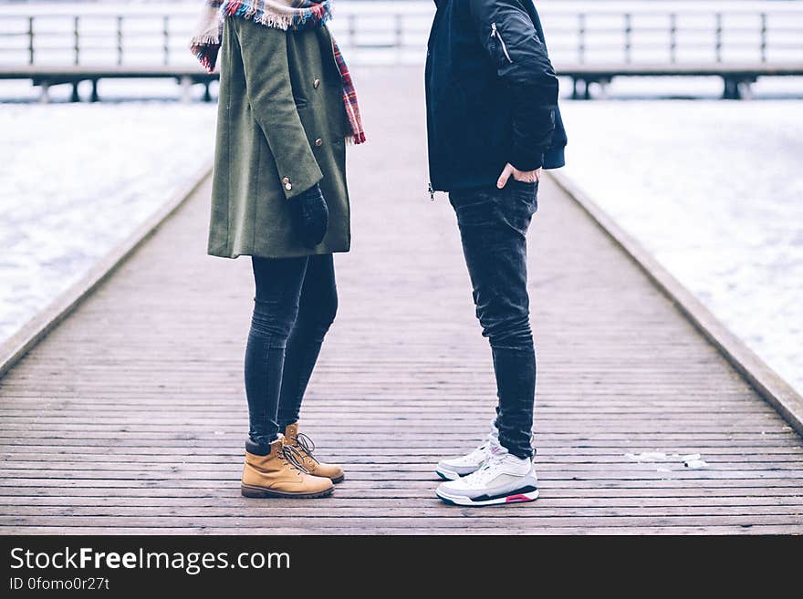 Couple dressed in warm clothes (showing bodies only) standing on a cobbled path at the seaside chatting, and in the background, seating on the promenade. Couple dressed in warm clothes (showing bodies only) standing on a cobbled path at the seaside chatting, and in the background, seating on the promenade.