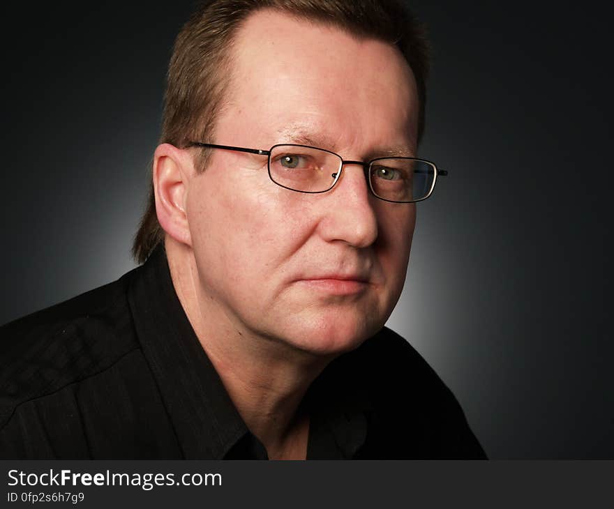 Closeup portrait of serious looking businessman or author wearing gold framed spectacles, dark background. Closeup portrait of serious looking businessman or author wearing gold framed spectacles, dark background.