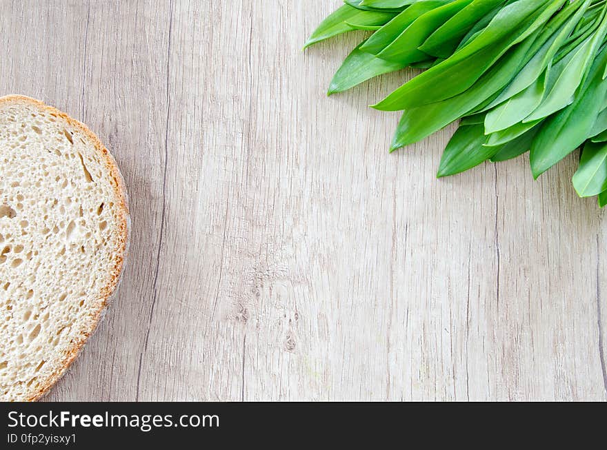 A slice of bread and leek leaves on a wooden surface.