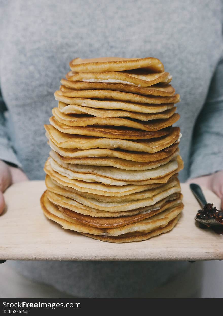 A person holding a wooden tray full of pancakes. A person holding a wooden tray full of pancakes.