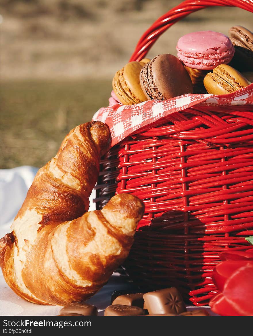 A picnic basket of French macarons and croissants with chocolates on the side. A picnic basket of French macarons and croissants with chocolates on the side.