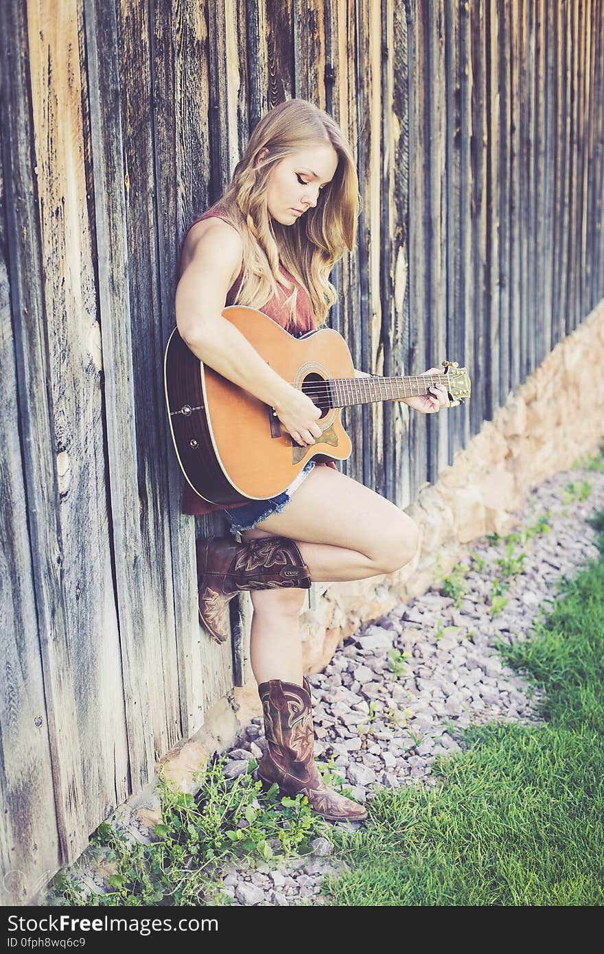 Woman Playing Guitar While Leaning on Wood during Daytime