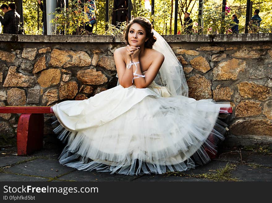 A woman in bridal gown sitting on a bench in the yard. A woman in bridal gown sitting on a bench in the yard.