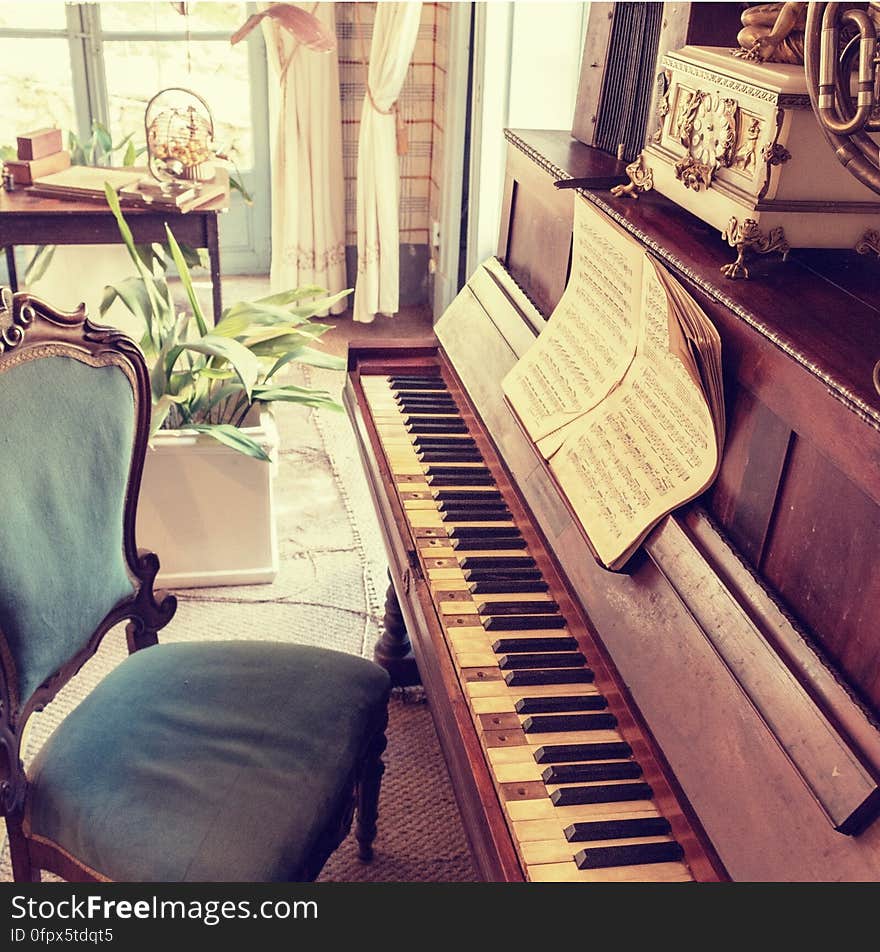 An old piano with note sheets and an empty chair beside it.