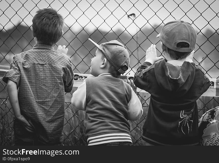 A black and white photo of three young boys standing by a wire fence. A black and white photo of three young boys standing by a wire fence.