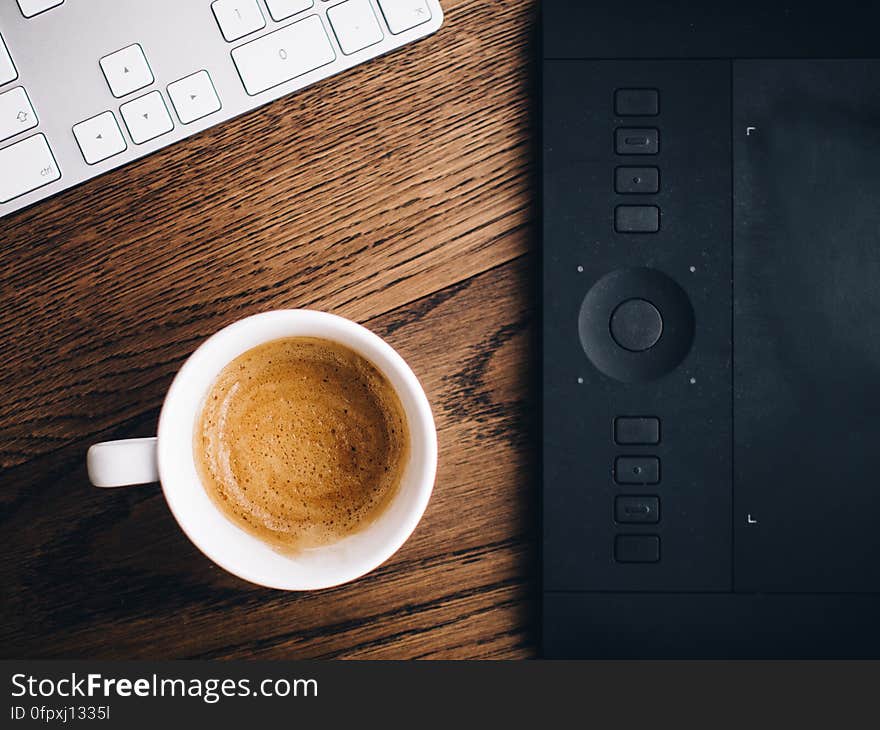 A cup of cappuccino next to a graphics tablet and computer keyboard. A cup of cappuccino next to a graphics tablet and computer keyboard.