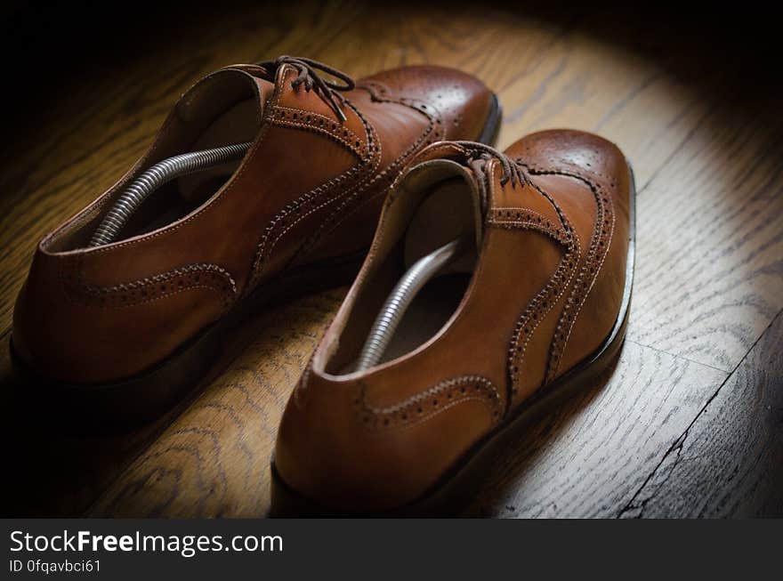 Pair of fashionable brown leather brogue shoes with shoe trees in them, grainy wooden background.