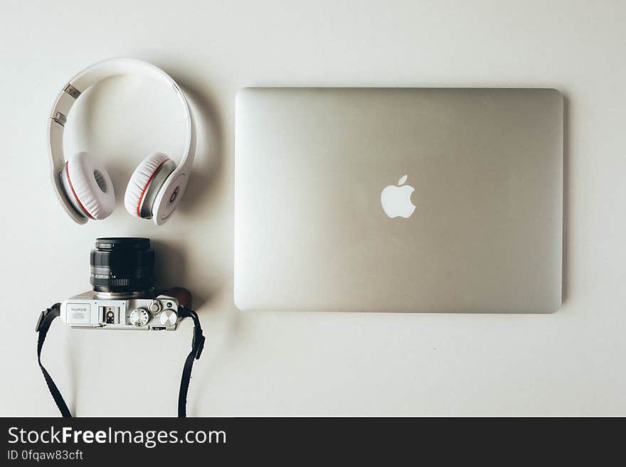 Apple laptop computer, elegant white headphones and retro film camera with strap, white background. Apple laptop computer, elegant white headphones and retro film camera with strap, white background.