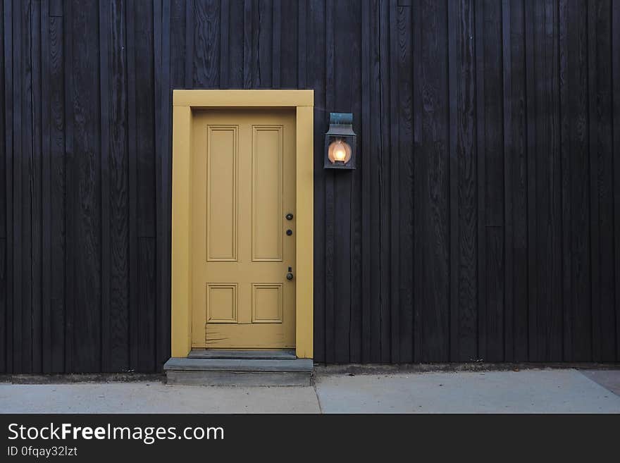 Black painted wooden house with paneled yellow (beige) painted door, blue slate step and gray path alongside. Black painted wooden house with paneled yellow (beige) painted door, blue slate step and gray path alongside.