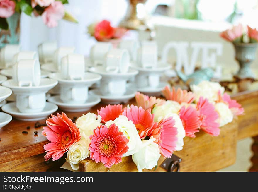 A set of white ceramic coffee cups and a flower arrangement on a wooden desk. A set of white ceramic coffee cups and a flower arrangement on a wooden desk.