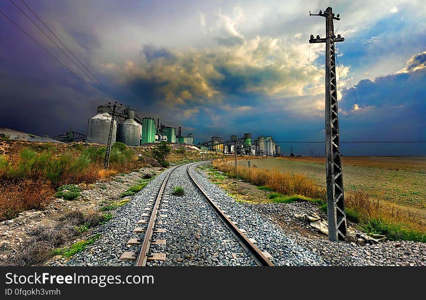 Scenic view of curving railway track receding past industrial engineering plant with towers and silos. Scenic view of curving railway track receding past industrial engineering plant with towers and silos.