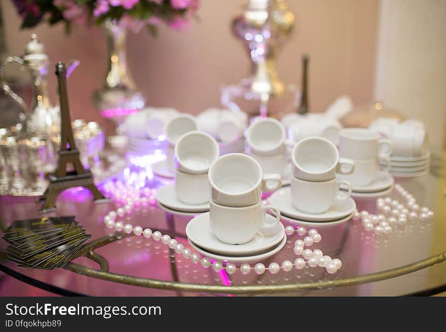 Ornamental tea set on glass table at wedding reception with model of Eiffel tower, flowers beads.