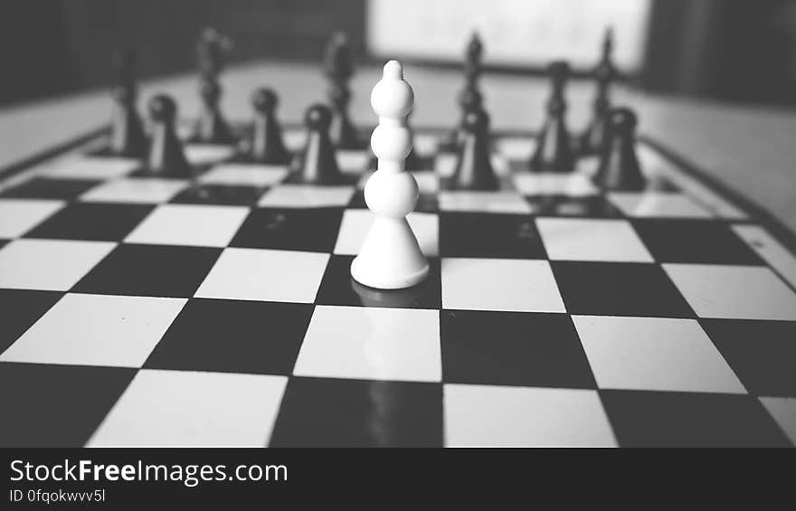 Closeup of white pawn on black square of chess board with preponderance of black pieces still in place. Closeup of white pawn on black square of chess board with preponderance of black pieces still in place.