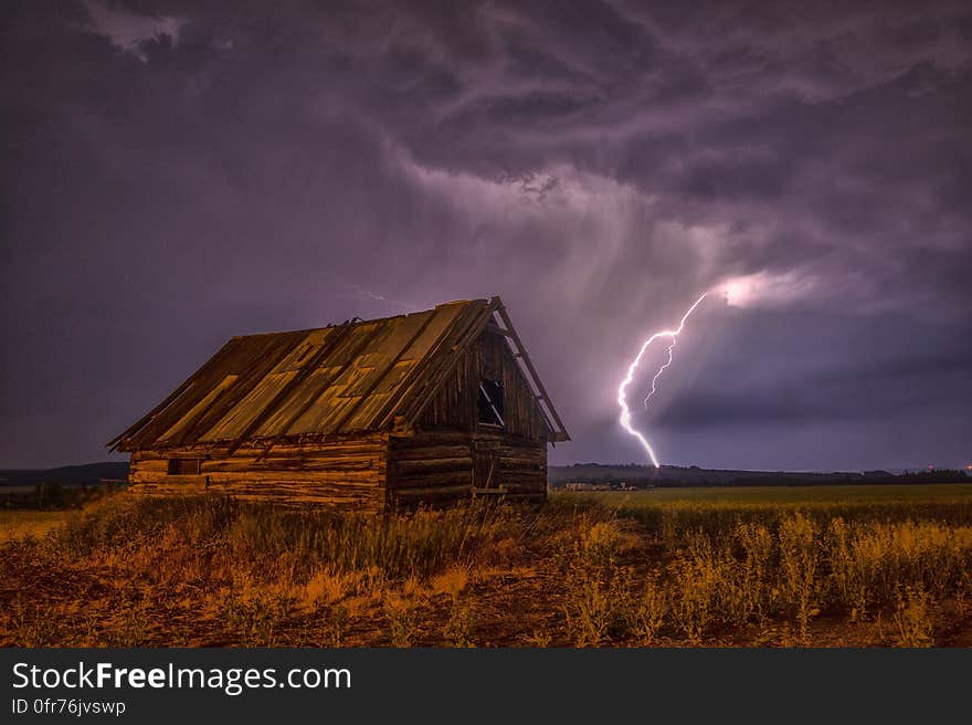 Brown and Beige Wooden Barn Surrounded With Brown Grasses Under Thunderclouds