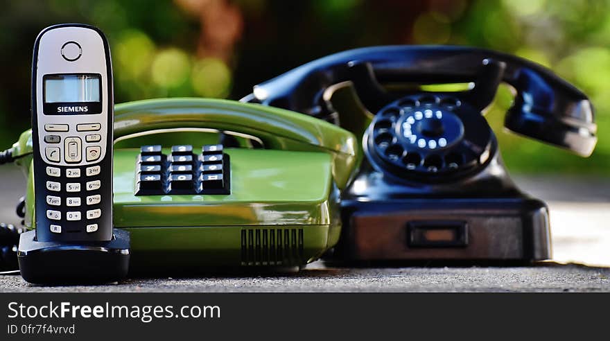 Black and Green Rotary Telephones Beside Cordless Home Telephone