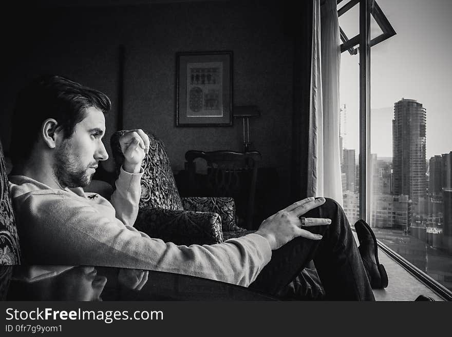 A pensive young man sitting by a window. A pensive young man sitting by a window.