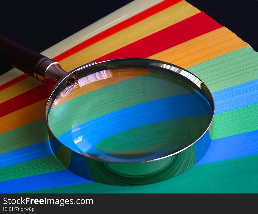 A fan of colorful sheets of papers and a magnifying glass on top. A fan of colorful sheets of papers and a magnifying glass on top.