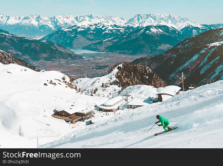 Skier on alpine slopes with resort in valley and mountain lake in horizon on sunny day. Skier on alpine slopes with resort in valley and mountain lake in horizon on sunny day.