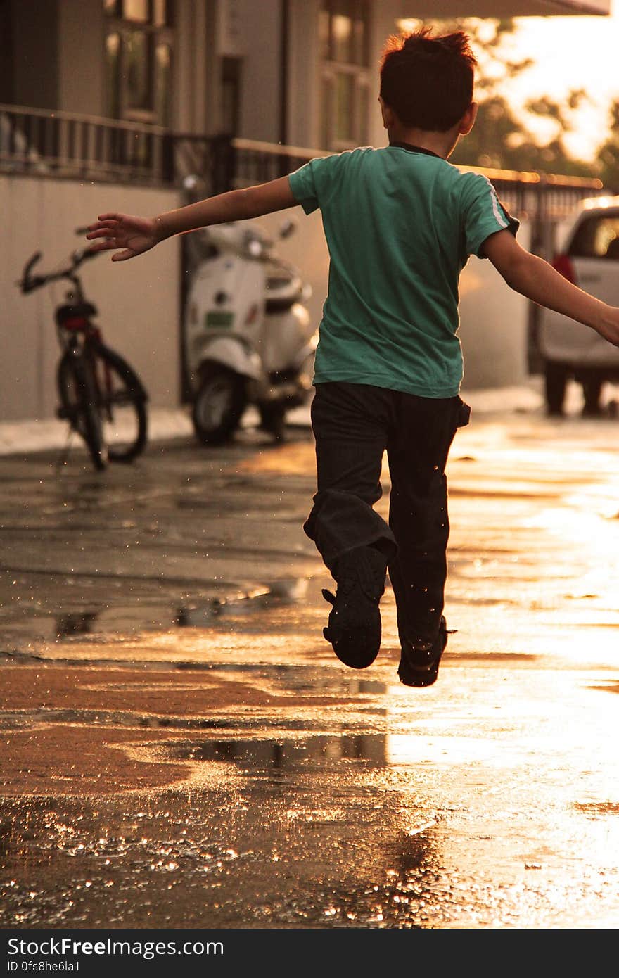 Boy in Green T Shirt Running on Wet Road during Daytime