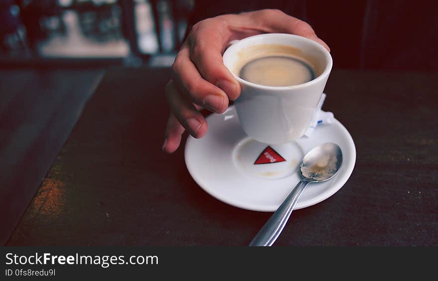 Hand of a person lifting cup of espresso coffee from saucer. Hand of a person lifting cup of espresso coffee from saucer.