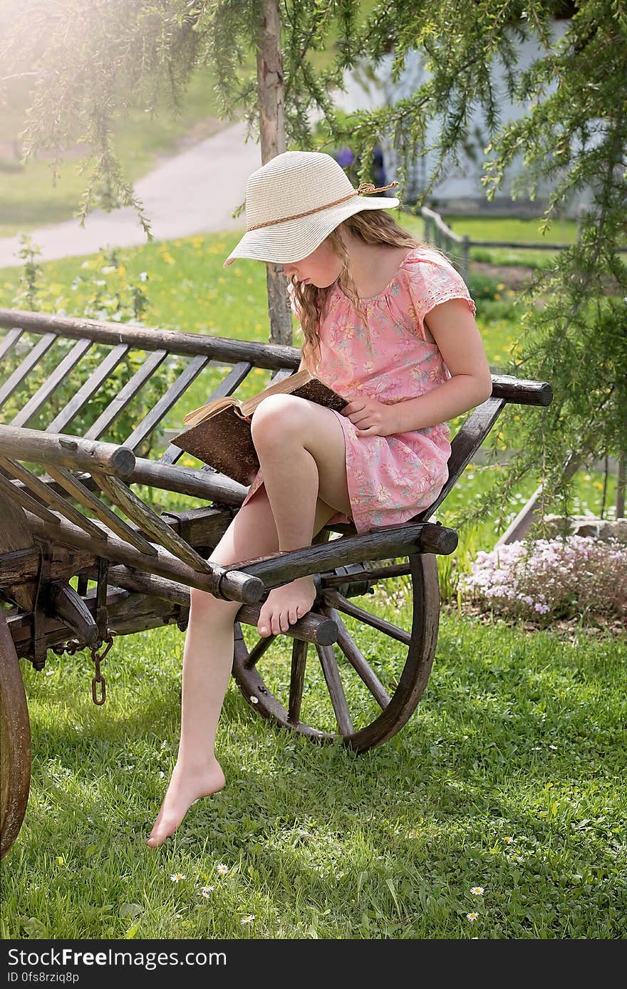 A girl sitting on an old wooden cart reading a book. A girl sitting on an old wooden cart reading a book.