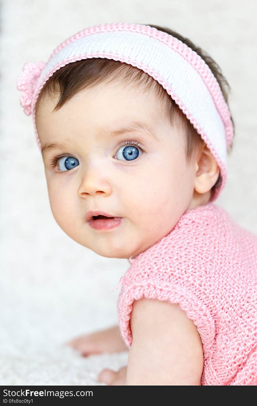 A baby with blue eyes and pink knitted headband and vest.