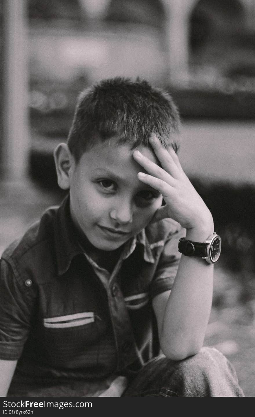 Black and white portrait of cute young boy outdoors with hand on forehead.