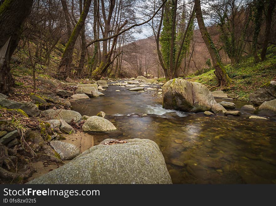 Stream with boulders on the banks flowing gently through woods in very early Spring. Stream with boulders on the banks flowing gently through woods in very early Spring.