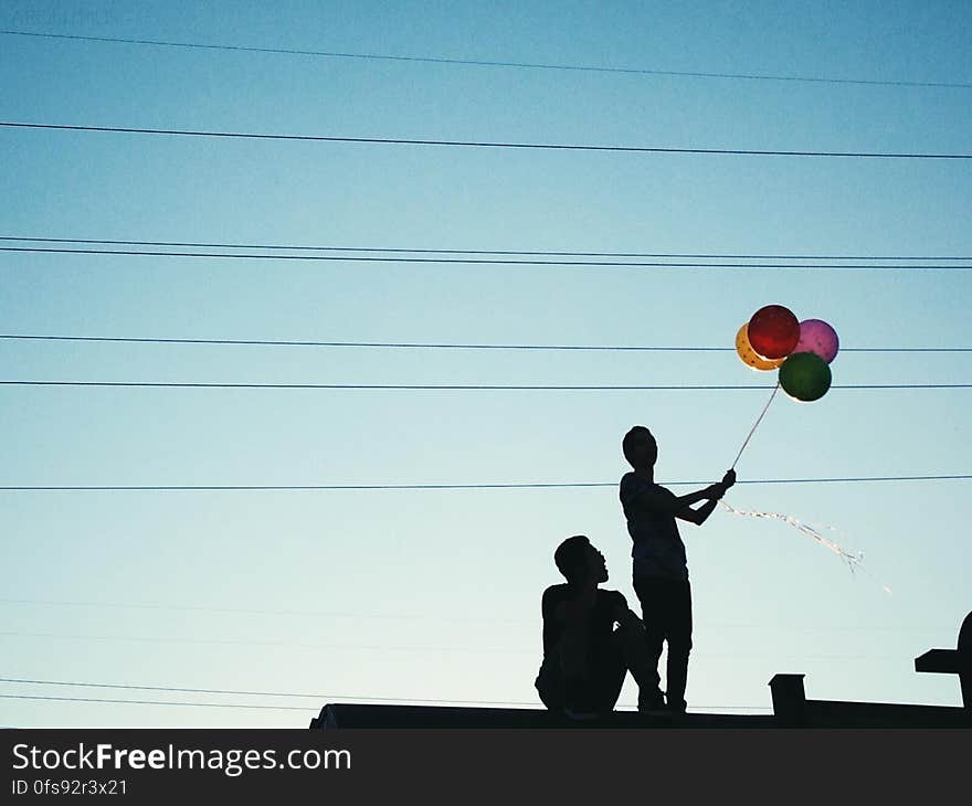 Men Holding Red Pink and Yellow Balloon Under Blue Sky during Daytime