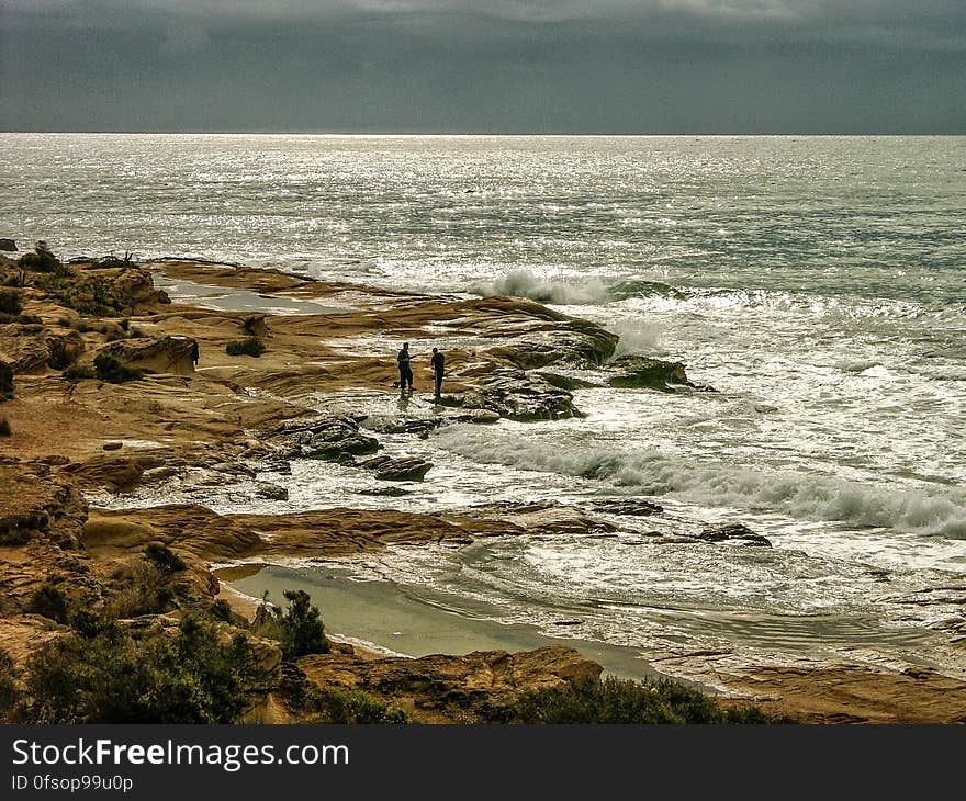 Two men standing on a rocky beach in the Mediterranean and open sea in the background. Two men standing on a rocky beach in the Mediterranean and open sea in the background.