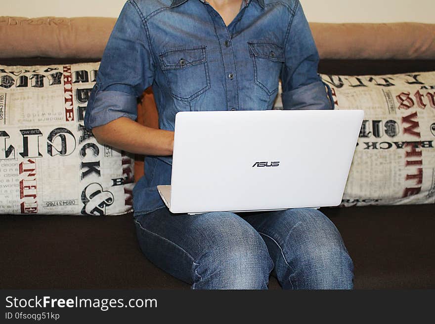 A woman sitting on sofa with denim outfit using a white laptop computer. A woman sitting on sofa with denim outfit using a white laptop computer.