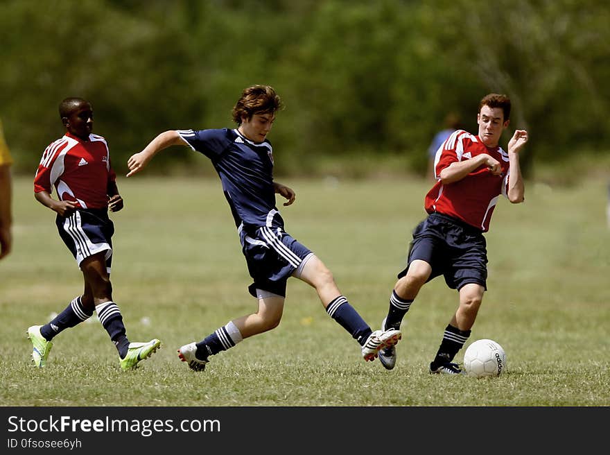 Three football players on a field running after the ball.