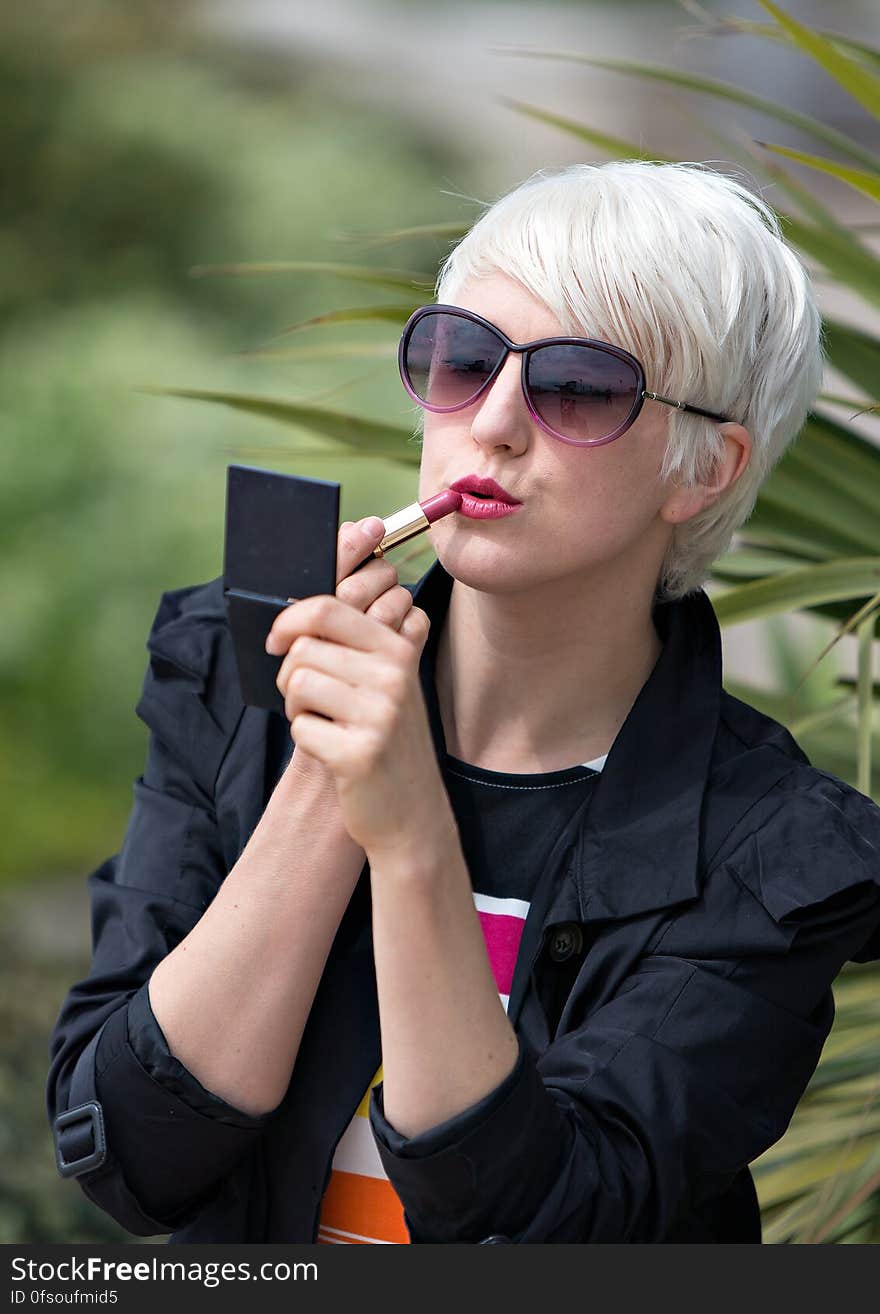 Blond Short Haired Woman Applying Pink Lipstick Outside