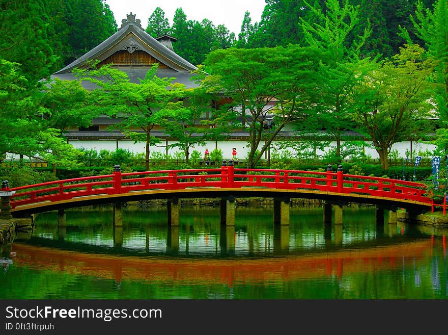 A red bridge over a pond in a garden and a traditional oriental temple in the background. A red bridge over a pond in a garden and a traditional oriental temple in the background.