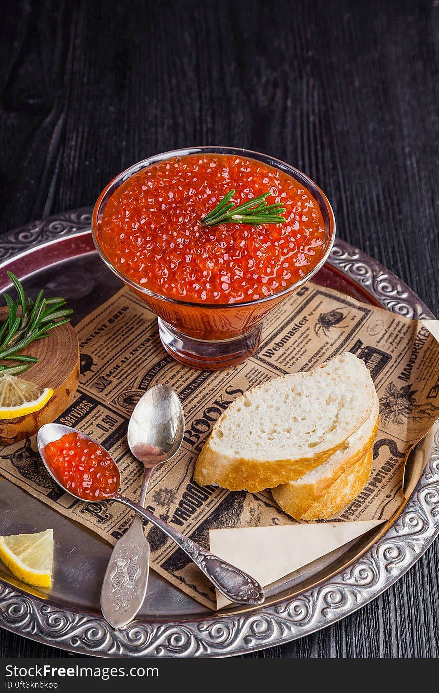 A cup of red fish roe and slices of bread and lemon with rosemary on a serving tray. A cup of red fish roe and slices of bread and lemon with rosemary on a serving tray.