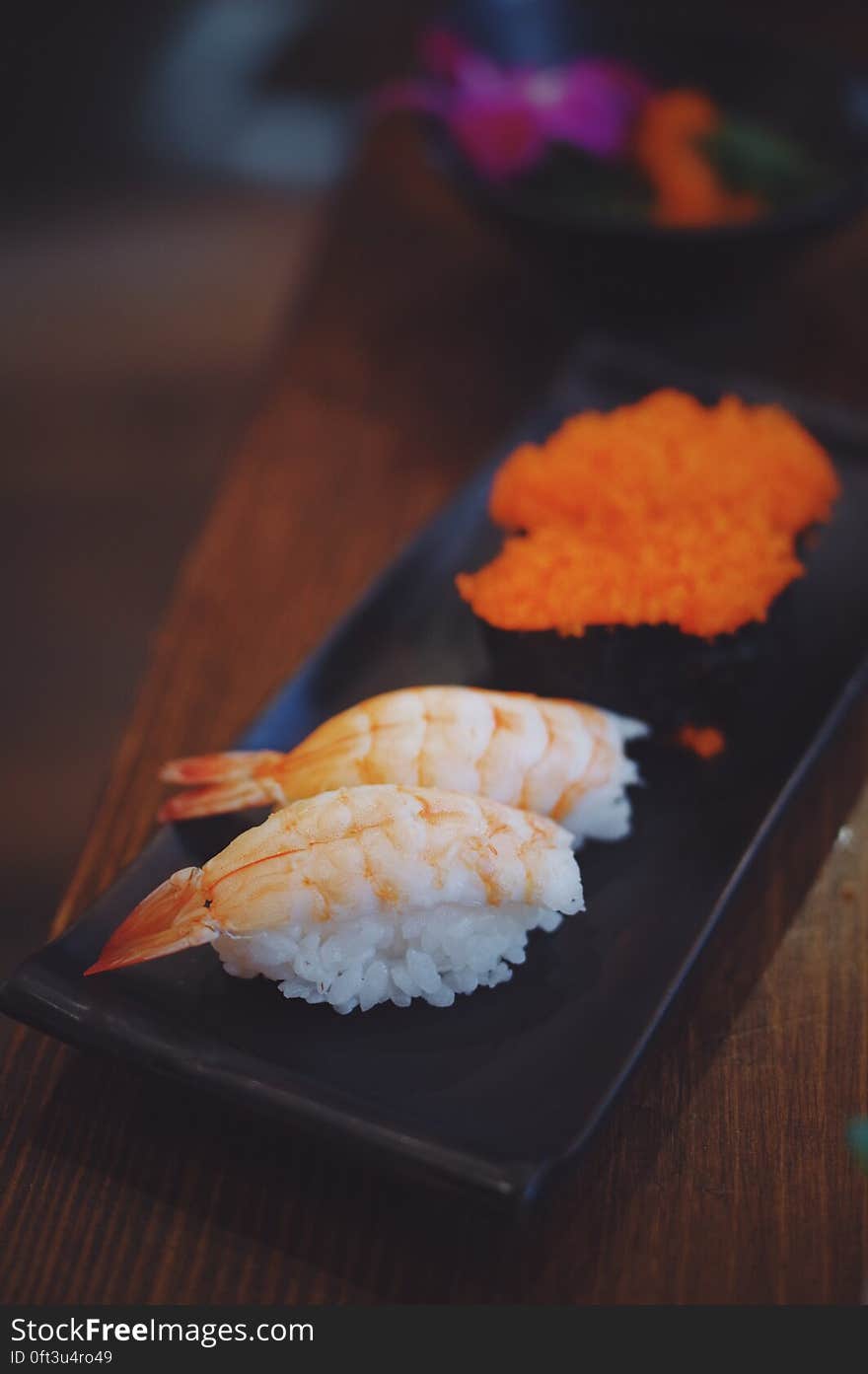 Close up of fresh prawns and salmon sushi on black plate on wooden table. Close up of fresh prawns and salmon sushi on black plate on wooden table.