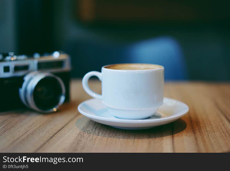 Still life of white china coffee cup and saucer on wooden tabletop with camera. Still life of white china coffee cup and saucer on wooden tabletop with camera.