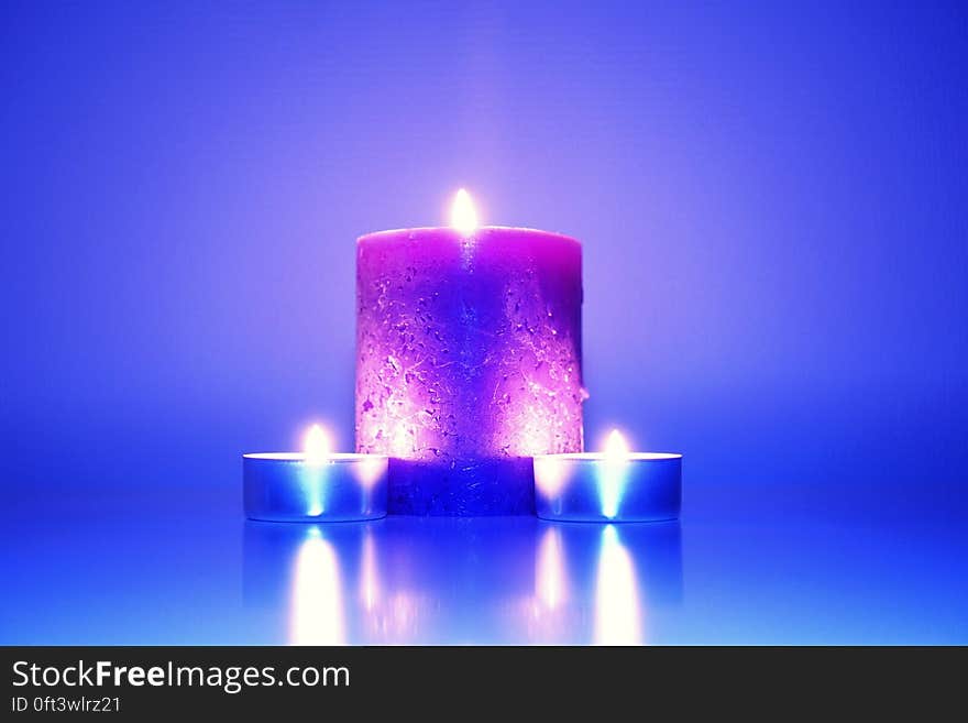 Low angle view of large and small candles reflecting on blue background. Low angle view of large and small candles reflecting on blue background.