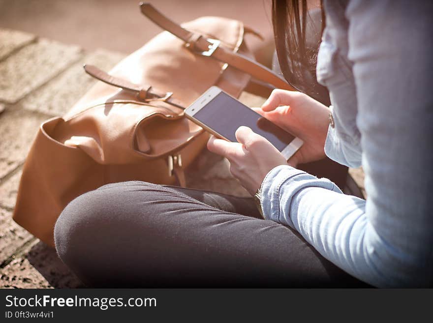 A girl with a leather bag sitting on pavement and using her mobile phone. A girl with a leather bag sitting on pavement and using her mobile phone.