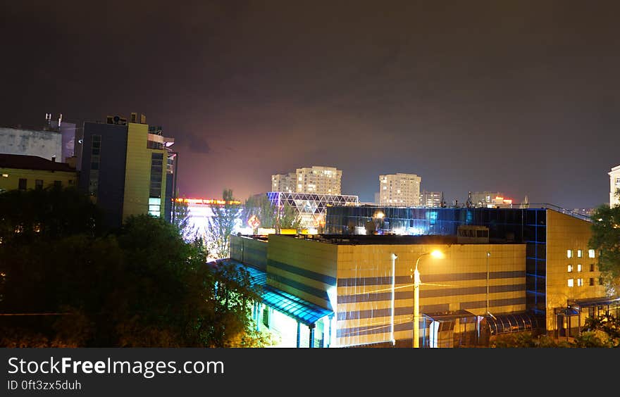 Aerial view over rooftops in urban skyline illuminated at night. Aerial view over rooftops in urban skyline illuminated at night.