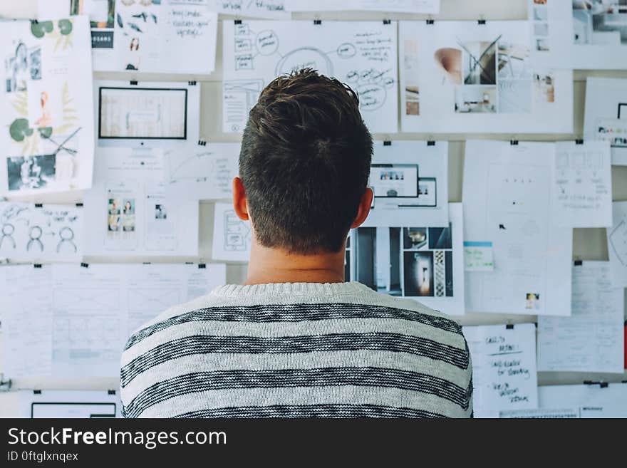 Man Wearing Black and White Stripe Shirt Looking at White Printer Papers on the Wall